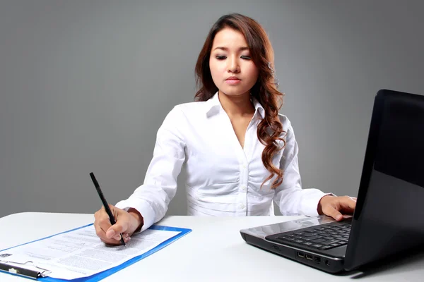 Jovem empresária escrevendo enquanto trabalhava com um laptop — Fotografia de Stock