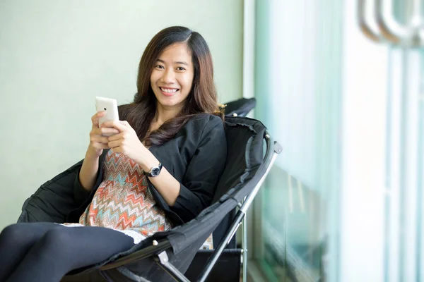 年轻的亚裔女子坐，用她的智能手机 — 图库照片