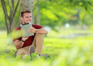 Üniversite öğrencisi ağacın altında oturan bir sekme oynarken zevk