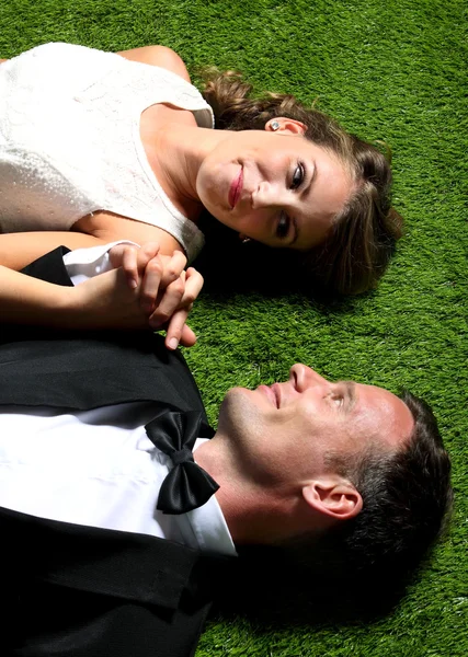 Bruid en bruidegom liggen op het gras terwijl elkaar de hand — Stockfoto