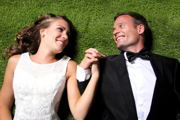 Newlywed couple lying on the grass and holding each other hands — Stock Photo, Image