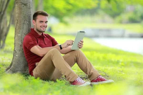 Studentów kolegium siedzący pod drzewem grając tabletki — Zdjęcie stockowe