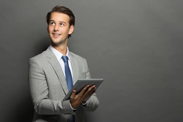 Young businessman thinking while holding a tablet — Stock Photo, Image