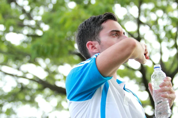 Jeune homme sportif boire de l'eau minérale pendant la pause après l'entraînement — Photo