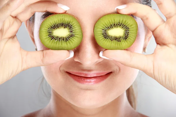 Beautiful woman holding kiwi fruits in front of her eyes — Stock Photo, Image