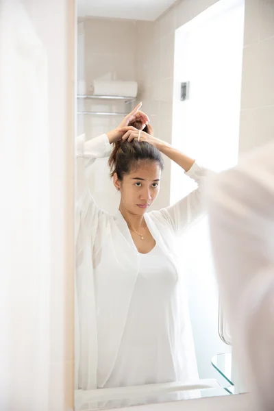 Красивая азиатская женщина аккуратно завязывает волосы перед зеркалом — стоковое фото
