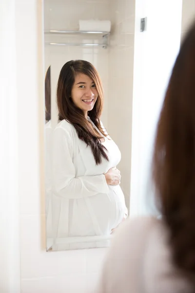 Asiática embarazada posando delante de un espejo, sonriendo feliz — Foto de Stock