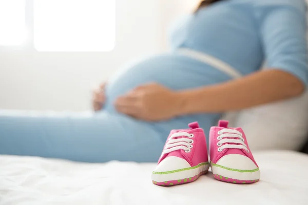 Un par de zapatillas rosadas al lado de una mujer embarazada, concéntrate o — Foto de Stock