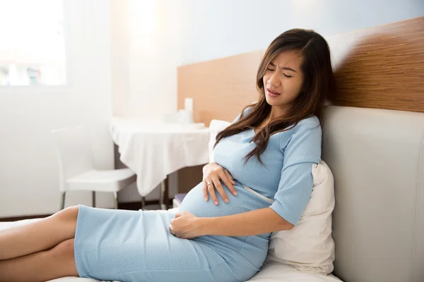 Asian pregnant woman has stomachache sitting on her bed — Stock Photo, Image