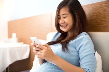 Güzel hamile kadın yatak odasında cep telefonu kullanıyor.