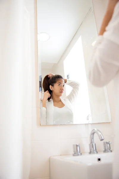Красива азіатська жінка зв'язує волосся, посміхаючись у дзеркалі — стокове фото
