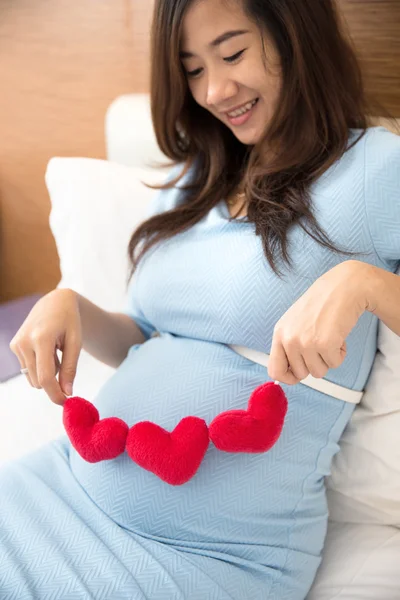 Asiatiska ung gravid kvinna sätta hjärtat formen tillbehör i sin tu — Stockfoto
