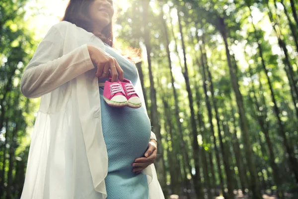 Pregnant woman holding a pair of pink sneakers baby shoes while — Stock Photo, Image
