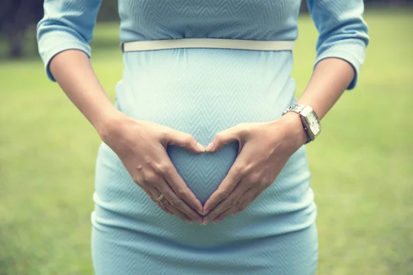 Mujer embarazada con el gesto de las manos en forma de corazón en el bulto del bebé —  Fotos de Stock