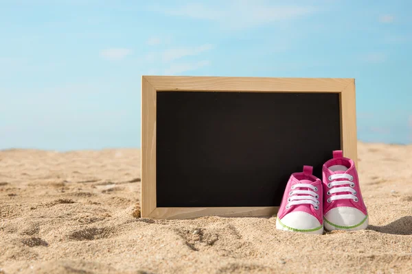 Chaussures pour tout-petits et mini tableau à craie sur le sable, concept de plage ba — Photo