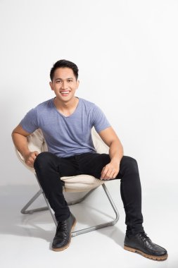 mutlu genç Asyalı adam beyaz arka plan üzerinde bir sandalyede oturuyor