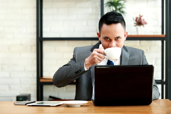 商人在办公室在笔记本电脑上工作时喝一杯咖啡 — 图库照片