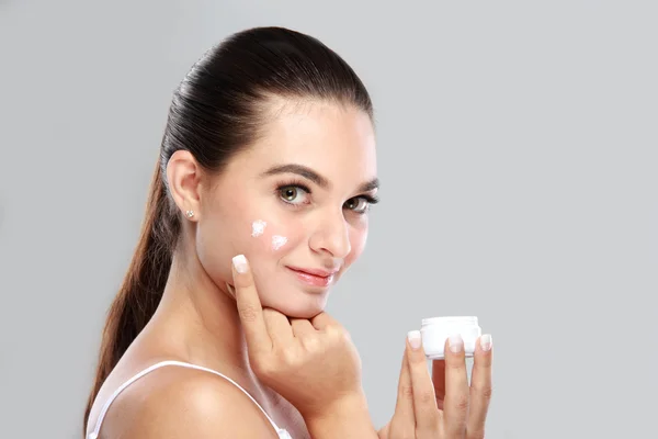 Hermosa joven aplicación de un poco de crema facial en su mejilla — Foto de Stock