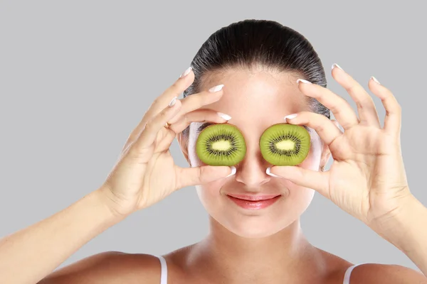 Young woman holding slices of kiwi in front of her eye — Stock Photo, Image