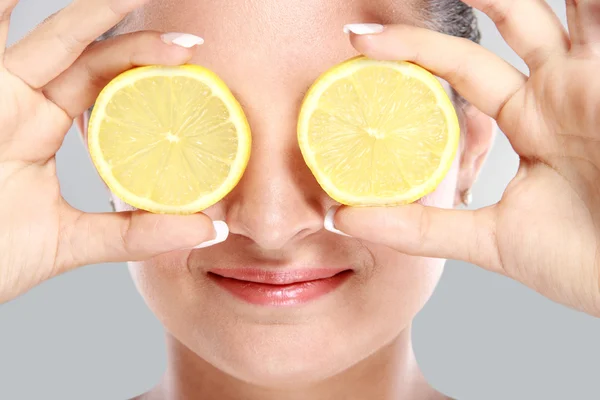 Woman smiling while holding slices of lemon in front of her eyes — Stock Photo, Image