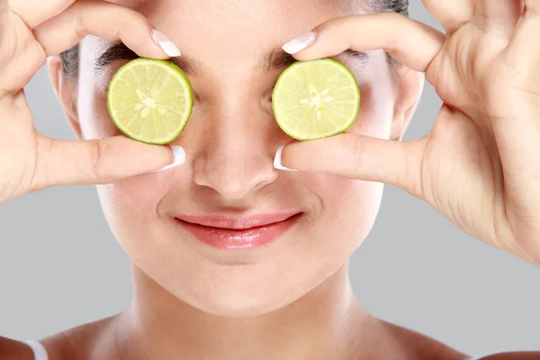 Beautiful woman holding slices of lime in front of her eyes — Stock Photo, Image