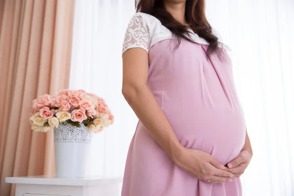 Vientre de la mujer embarazada con un vestido rosa — Foto de Stock