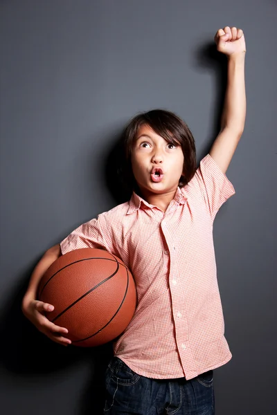 Веселий маленький хлопчик підняв руку і тримає баскетбол — стокове фото