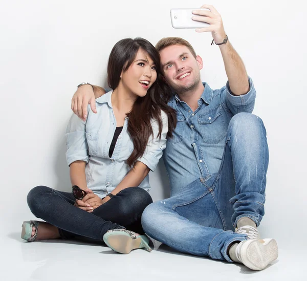 Mixed couple sitting on the floor taking self camera together — Stockfoto