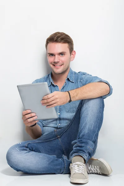 Young caucasian man sitting on the floor holding a tablet pc — Stock Photo, Image
