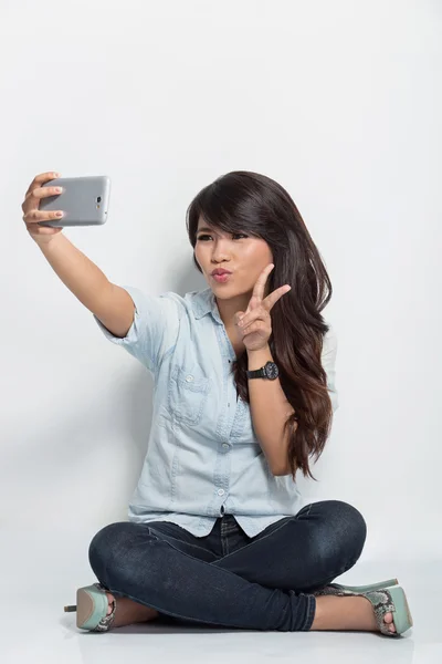 Young woman sitting on the floor taking self camera — Stockfoto