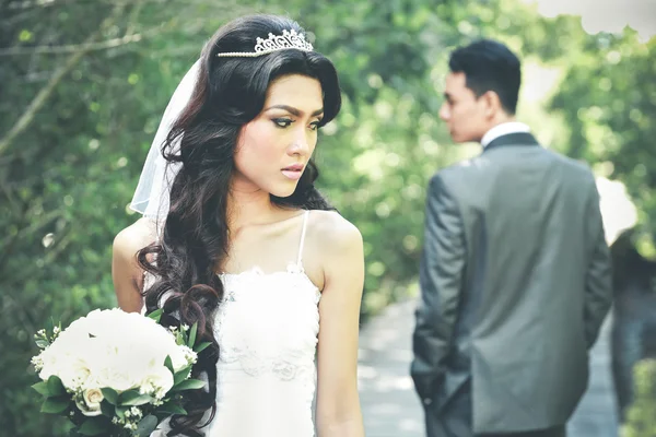 Braut blickt zurück, während sie einen Strauß mit ihrem Bräutigam bei beh hält — Stockfoto