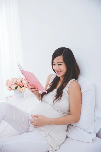 Schöne schwangere asiatische Frau liest Notizbuch und lächelt — Stockfoto