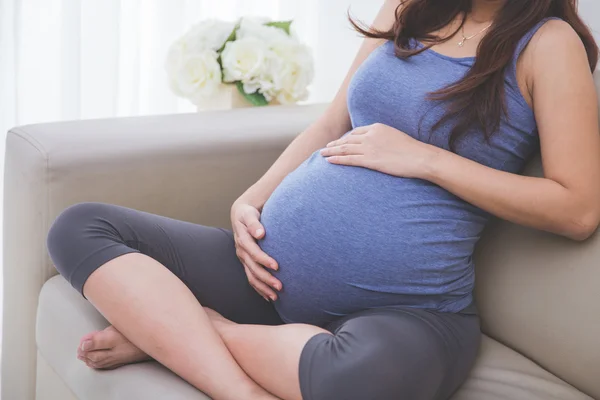 Donna incinta seduta sul divano, da vicino sullo stomaco — Foto Stock