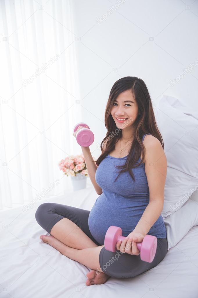 Beautiful asian pregnant woman doing exersice on her bed