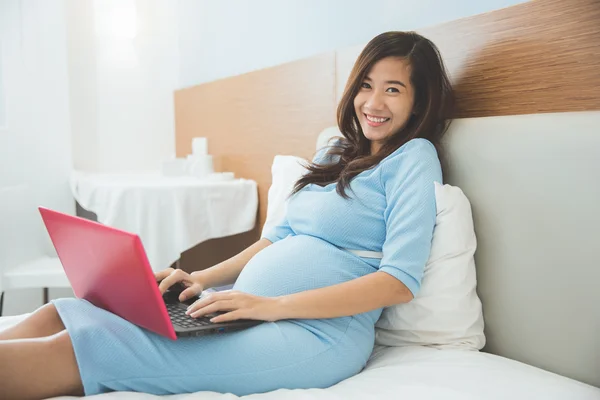 Aziatische zwangere vrouw met laptop op het bed, glimlach en ontspannen — Stockfoto