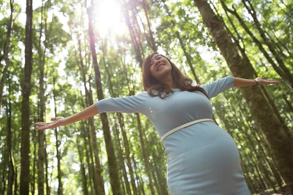 Mujer joven embarazada disfrutando del bosque con los brazos abiertos — Foto de Stock