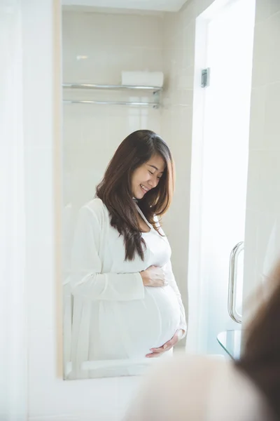 Asian pregnant woman posing in front of a mirror, smiling proudl — Stock Photo, Image