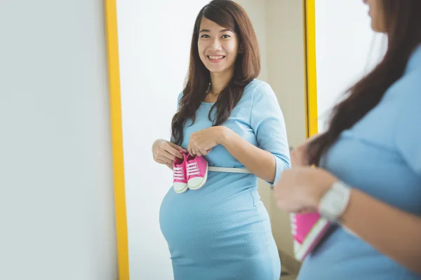 Mujer embarazada sonriendo delante de un espejo, sosteniendo un par de b — Foto de Stock