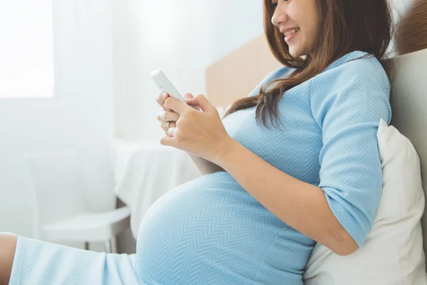 아름다운 임신부가 침실에서 휴대 전화를 사용하는 모습 — 스톡 사진