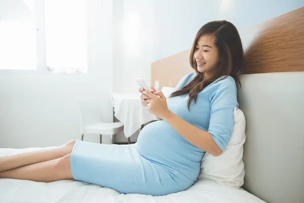 Bella donna incinta utilizzando il telefono cellulare nella sua camera da letto — Foto Stock