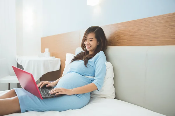 Aziatische zwangere vrouw met laptop op het bed, glimlach en ontspannen — Stockfoto