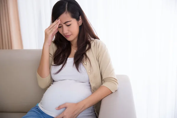 Pregnant asian woman got headache, sitting on a couch — Stock Photo, Image