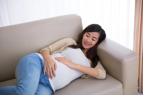 Беременная азиатка лежит на диване — стоковое фото