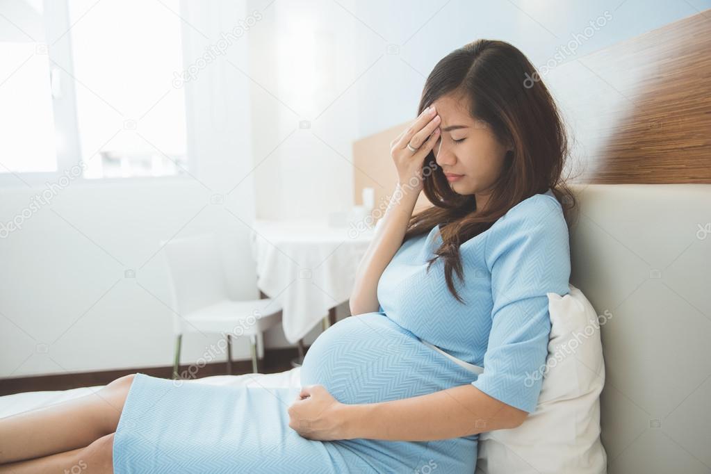 Asian pregnant woman has headache sitting on her bed