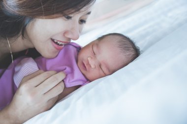 Young mother laying her newborn sleeping babyon bed, close up