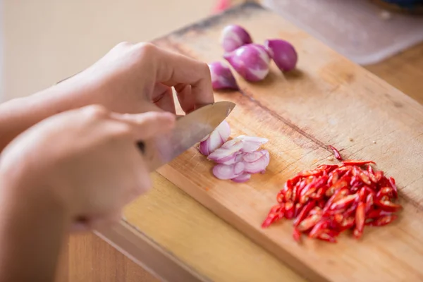 Manos rebanando cebolla roja y chile sobre tabla de cortar de madera — Foto de Stock