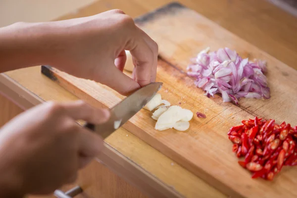 Hände schneiden Zwiebel, Knoblauch und Chili auf einem Holzschneidebrett — Stockfoto