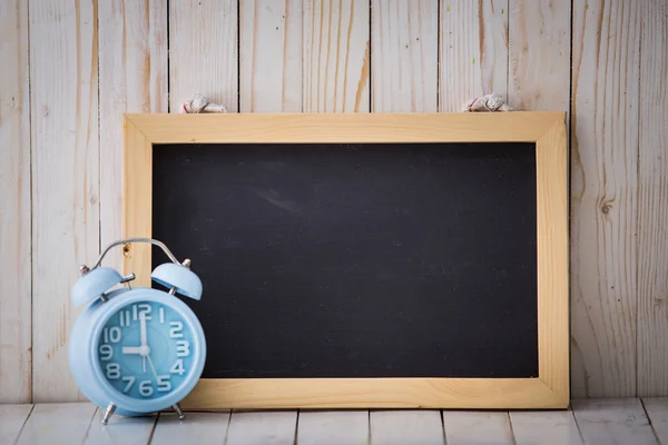 Chalkboard and blue alarm clock on wooden background — Stock Photo, Image