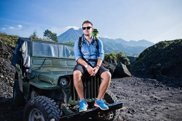 Stilig ung kaukasiska man sitter på huven på en jeep, berg — Stockfoto