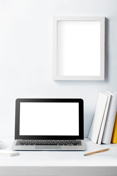 Portátil en el escritorio de trabajo y el marco en la pared blanca —  Fotos de Stock